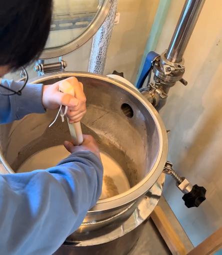 参加者が麦芽をお湯に浸して糖化させる「マッシング」の工程を、仕込みタンクの上から真剣に覗き込んでいる様子
