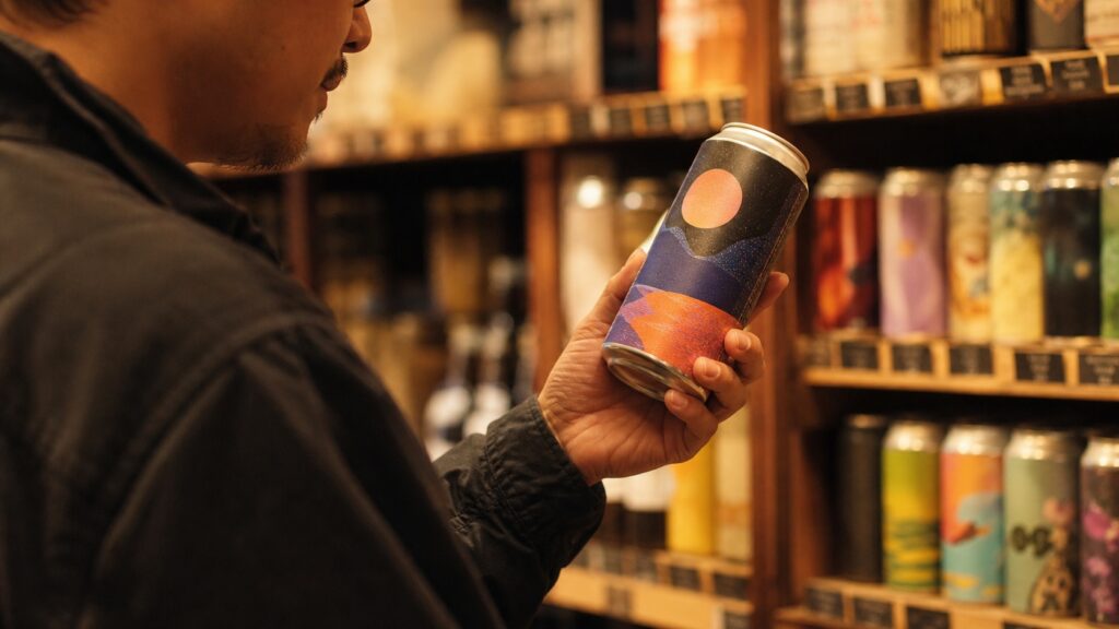 クラフトビールの缶を手に取って眺めている酒屋の店頭のシーン